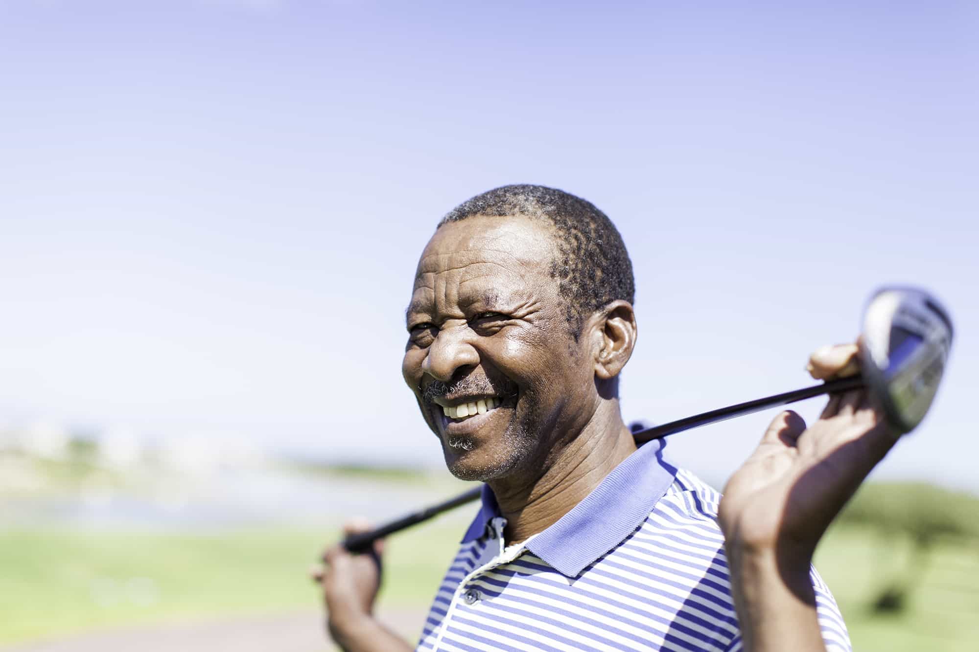 Someone holding a golf club and smiling near our 55 and over apartments in Cypress, featuring blue skies and a golf course