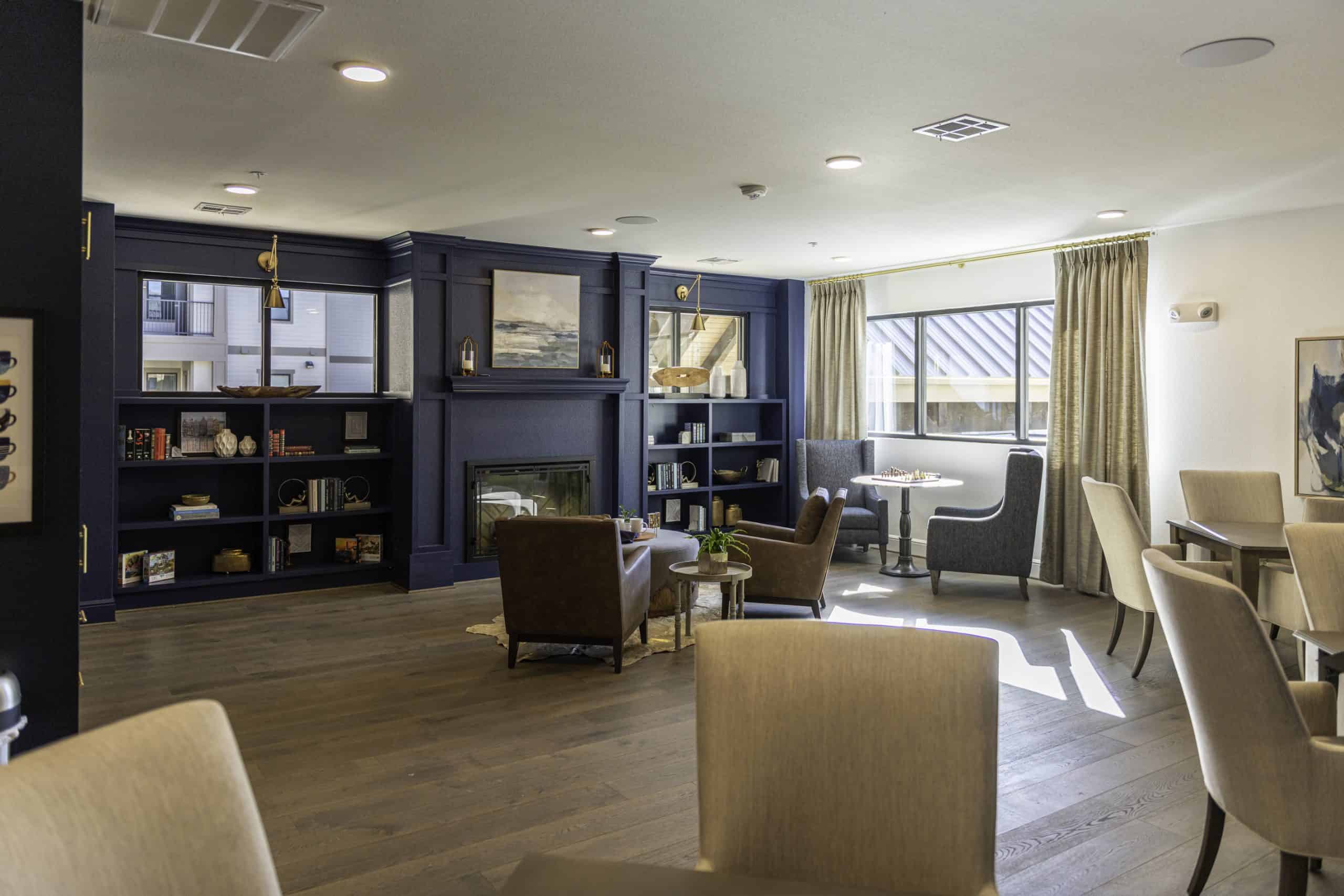 Lounge at our senior living community in Cypress, TX, featuring cushioned chairs, book shelves, and a fireplace.