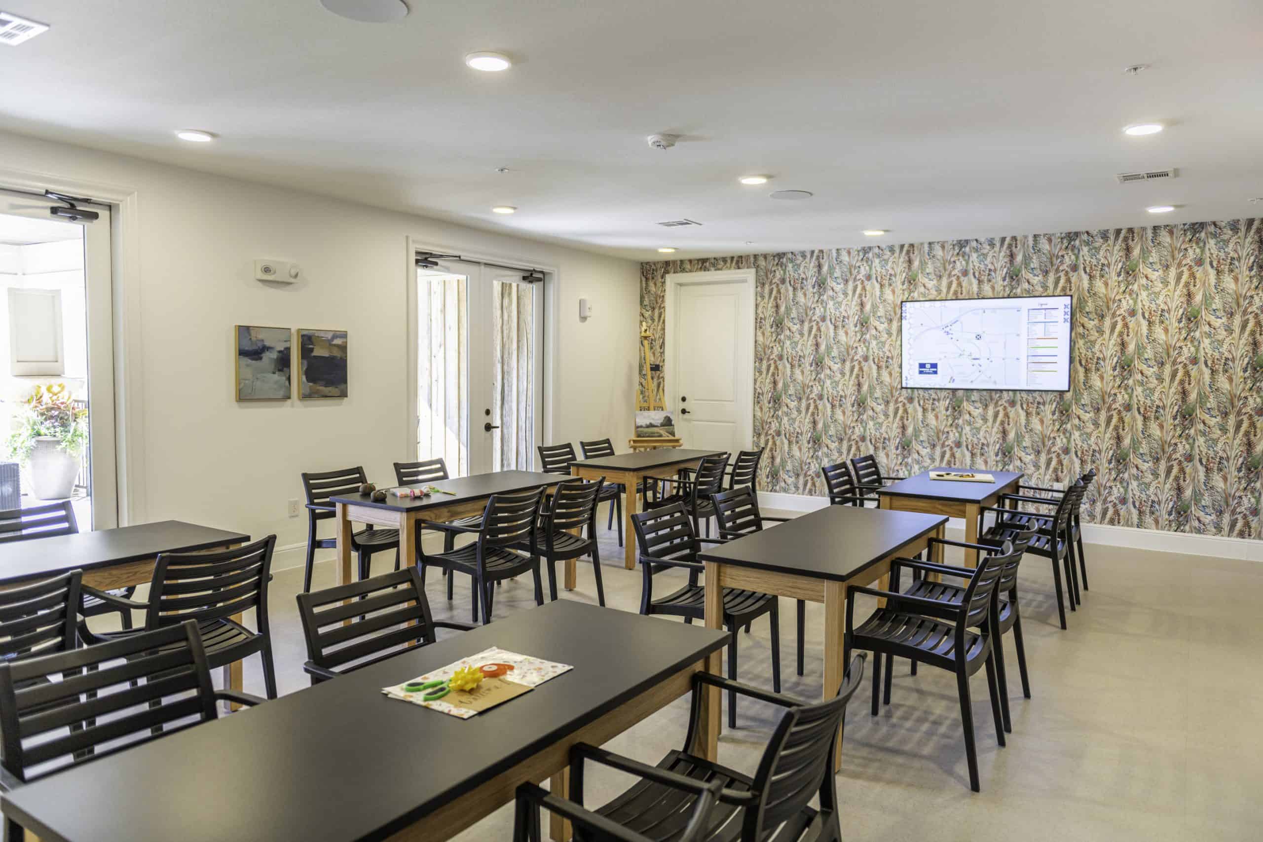 Community and event space at our 55 plus apartments in Cypress, TX, featuring tables, chairs, and a TV.