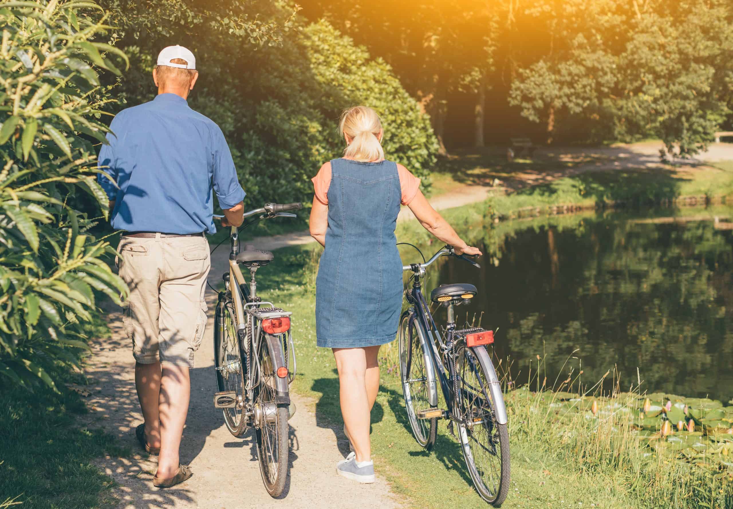 Two people walking their bikes along a path near our 55 plus community in Cypress, featuring a pond.